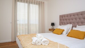 A neatly made bed with rolled towels, a tufted headboard, and a nightstand with a lamp. - Pata da Gaivota Boutique House (Lourinha)