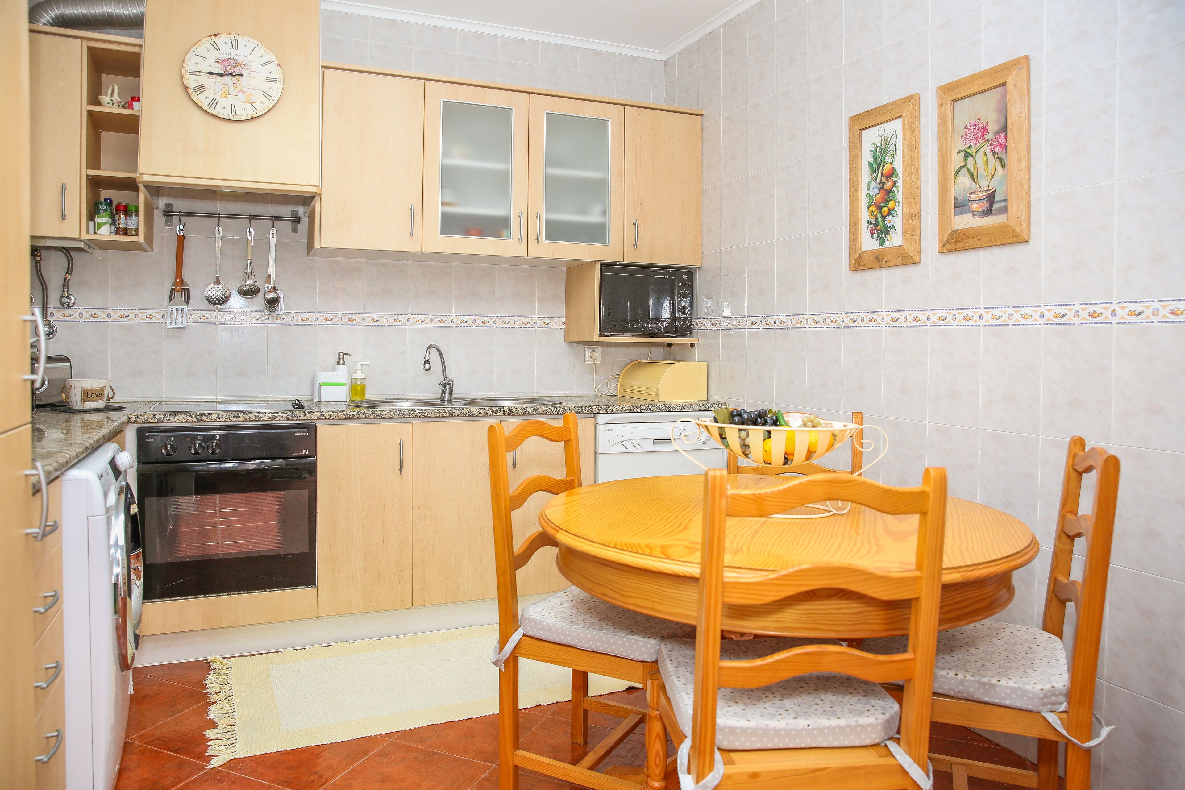 Una cocina con armarios de madera, un microondas, una estufa y una mesa de comedor con sillas.