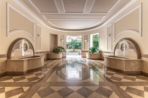 Um hall amplo com piso xadrez, duas pias grandes e vista para o exterior.