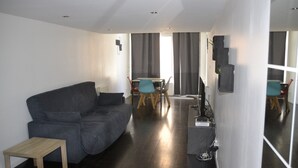 Un salon moderne avec un canapé gris, une petite table en bois et un coin repas comprenant des chaises et une table.