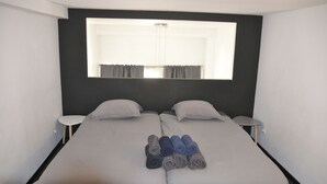 Un lit double avec deux tables de chevet, une fenêtre avec des rideaux et un ensemble de serviettes sur le lit.