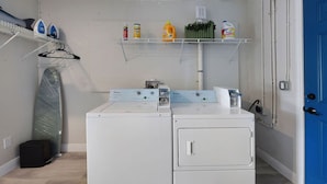 A laundry room with two white washing machines, a drying rack, and shelves with cleaning supplies.