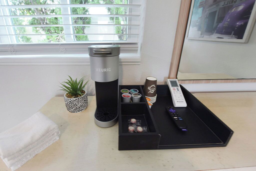 A coffee maker, a remote control, and a tray with coffee pods on a table near a window.