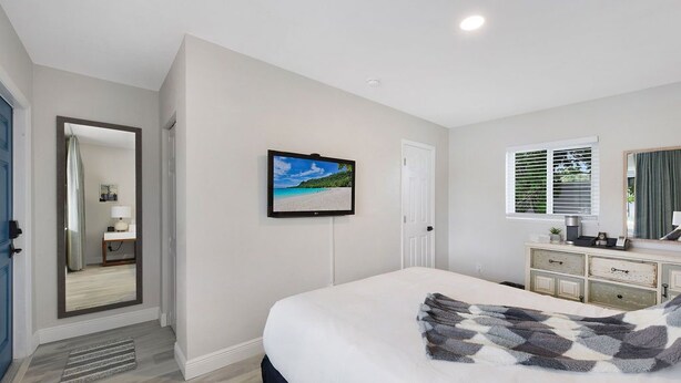 A bedroom with a bed, a television, a dresser, and a window with blinds.