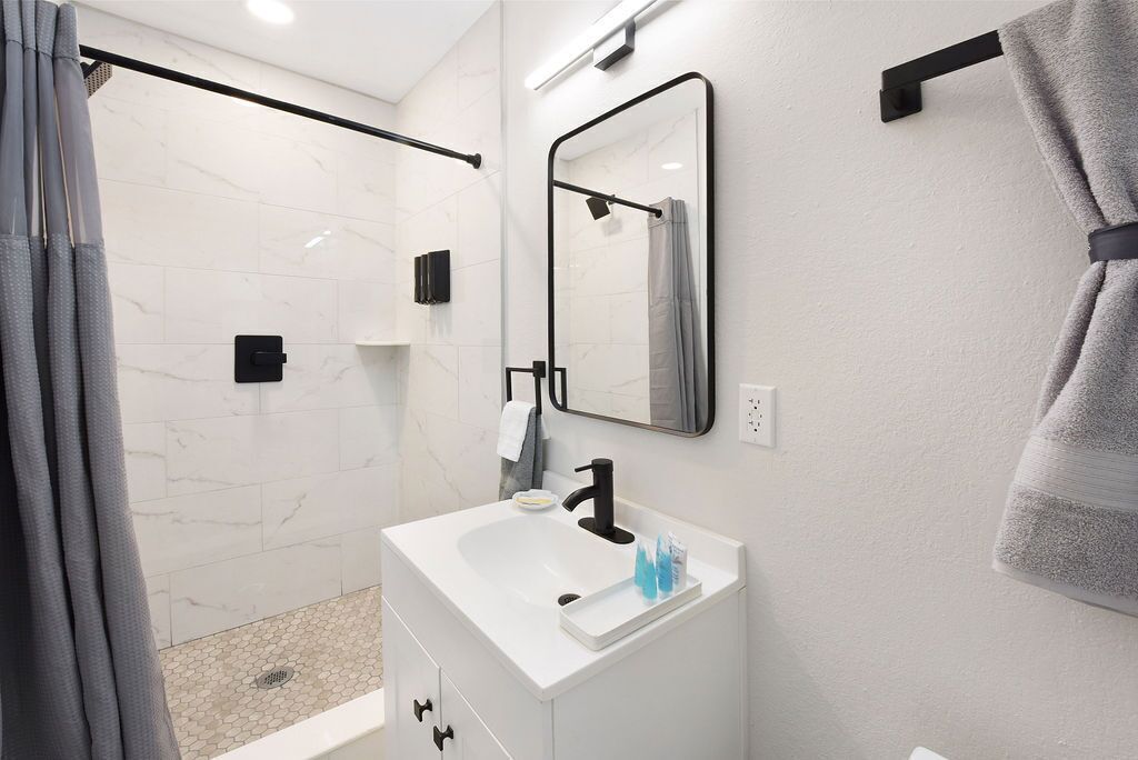 Une salle de bain moderne avec un lavabo blanc, un robinet noir et un miroir au-dessus.