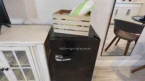 A black refrigerator with the word "Refresh" on top and "Frigidaire" on the side, placed next to a white cabinet with glass doors. - Deluxe Room with Queen Bed and Kitchenette (Clearwater)