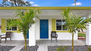 Un bâtiment avec une porte bleue, deux chaises à l’extérieur et des plantes devant.