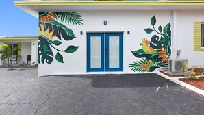 Un bâtiment avec une porte bleue et une fresque représentant des feuilles et des oiseaux tropicaux sur le côté.
