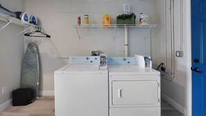 Une buanderie équipée de deux machines à laver blanches, d’un étendoir et d’étagères contenant des produits de nettoyage.
