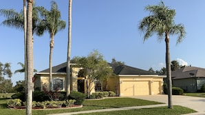 Una casa residencial con garaje, rodeada de céspedes cuidados y palmeras.