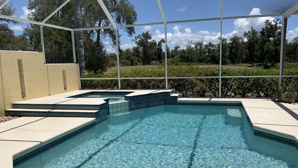 Una piscina azul clara con escalones de cerámica, rodeada por una cerca blanca y árboles al fondo.