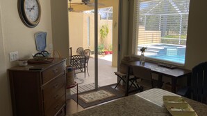 Una cocina con encimera de granito, un comedor con sillas de mimbre, un ventilador de techo y vista a una piscina por la ventana.