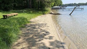 En sandstrand med en träbänk och en båt i bakgrunden.