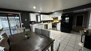 Una cucina moderna con mobili bianchi, un frigorifero nero e un'area pranzo con tavolo e sedie in legno.