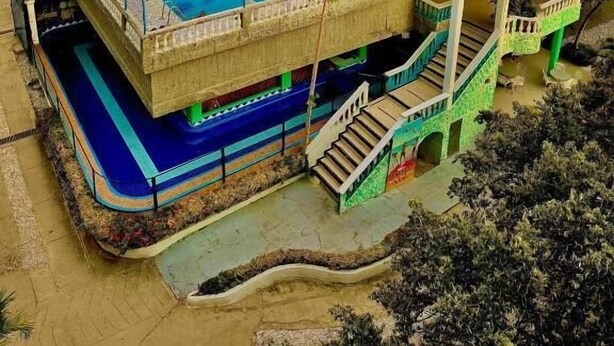 A hotel with a large swimming pool, multiple floors, and a tower with a blue roof.