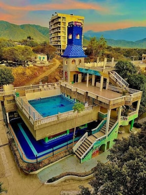 A hotel with a large swimming pool, multiple floors, and a tower with a blue roof. - SGH Hotel Castillo Aqua (Santa Marta)
