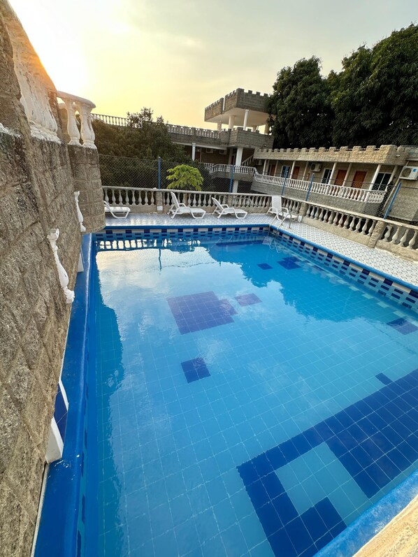 A swimming pool with a stone wall and a balcony with white railings. - SGH Hotel Castillo Aqua (Santa Marta)