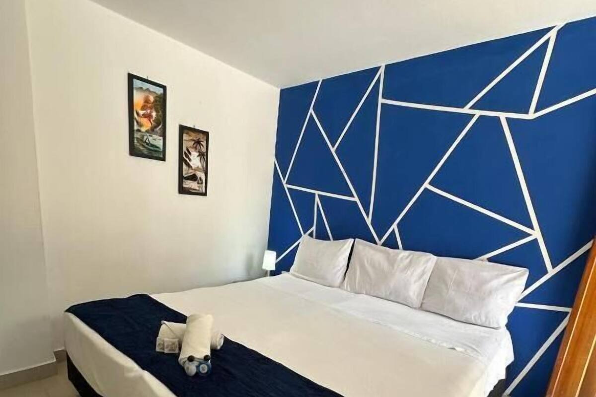 Et hotelværelse med en seng, en blå sengegavl med geometrisk mønster, og to billeder hængende på væggen.