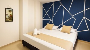 A neatly made bed with white and beige bedding, a geometric-patterned headboard, and a small framed picture on the wall.