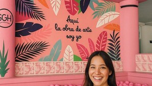 A room with a pink ball pit and a wall decorated with colorful leaf patterns and the text "Aquí la obra de arte soy yo".
