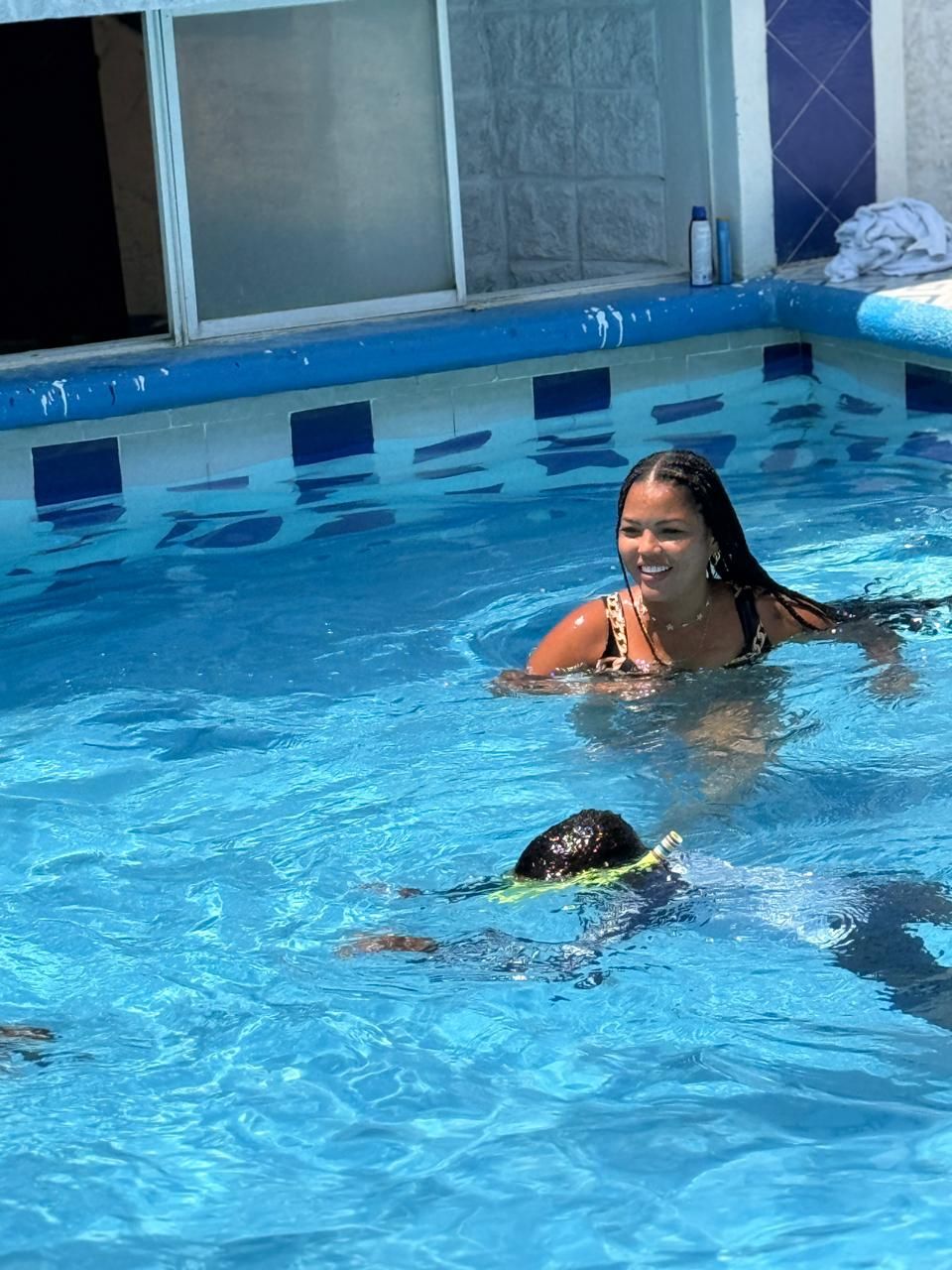 En swimmingpool med klart, blåt vand, fliset kant og en person i vandet.