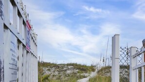 Ein begrenzter Eingang mit einem Weg, der zu einer Sandfläche führt, umgeben von Vegetation.