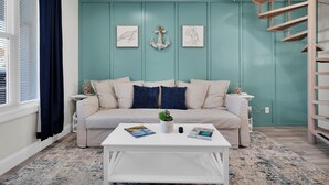 Ein Wohnzimmer mit einer Türkis-farbenen Akzentwand, einem weißen Sofa, einem Couchtisch und einer Wendeltreppe.