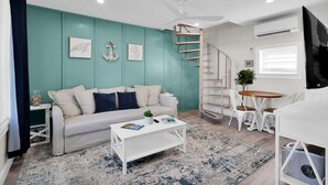 Ein modernes Wohnzimmer mit türkisfarbenen Wänden, einem weißen Sofa, einem Couchtisch und einer Wendeltreppe.