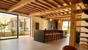 A spacious kitchen with a central island, wooden beams, and a large sliding glass door leading to an outdoor area.