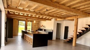 A modern kitchen with a central island, wooden beams on the ceiling, and a view of the outdoors. - Gite Le Biau Classé 5 Étoiles, Piscine, Campagne Gers (Castillon-Debats)