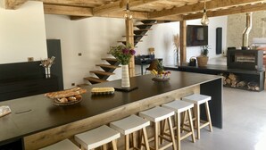 A modern kitchen with a wooden ceiling, a central island with stools, a built-in stove, and a staircase leading to an upper level.