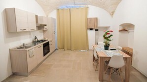 Une cuisine compacte avec un coin repas, comprenant une petite table et des chaises, une plante en pot et un porte-manteau suspendu.