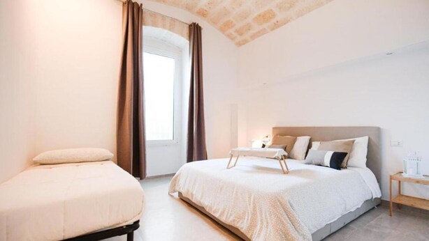Une chambre à coucher avec un lit, une table de chevet, une fenêtre avec des rideaux et un plafond en briques.