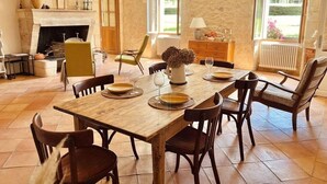 Un comedor con una mesa de madera dispuesta para cuatro personas, rodeada de sillas. Se ve una chimenea al fondo y un ventanal grande que proporciona luz natural.