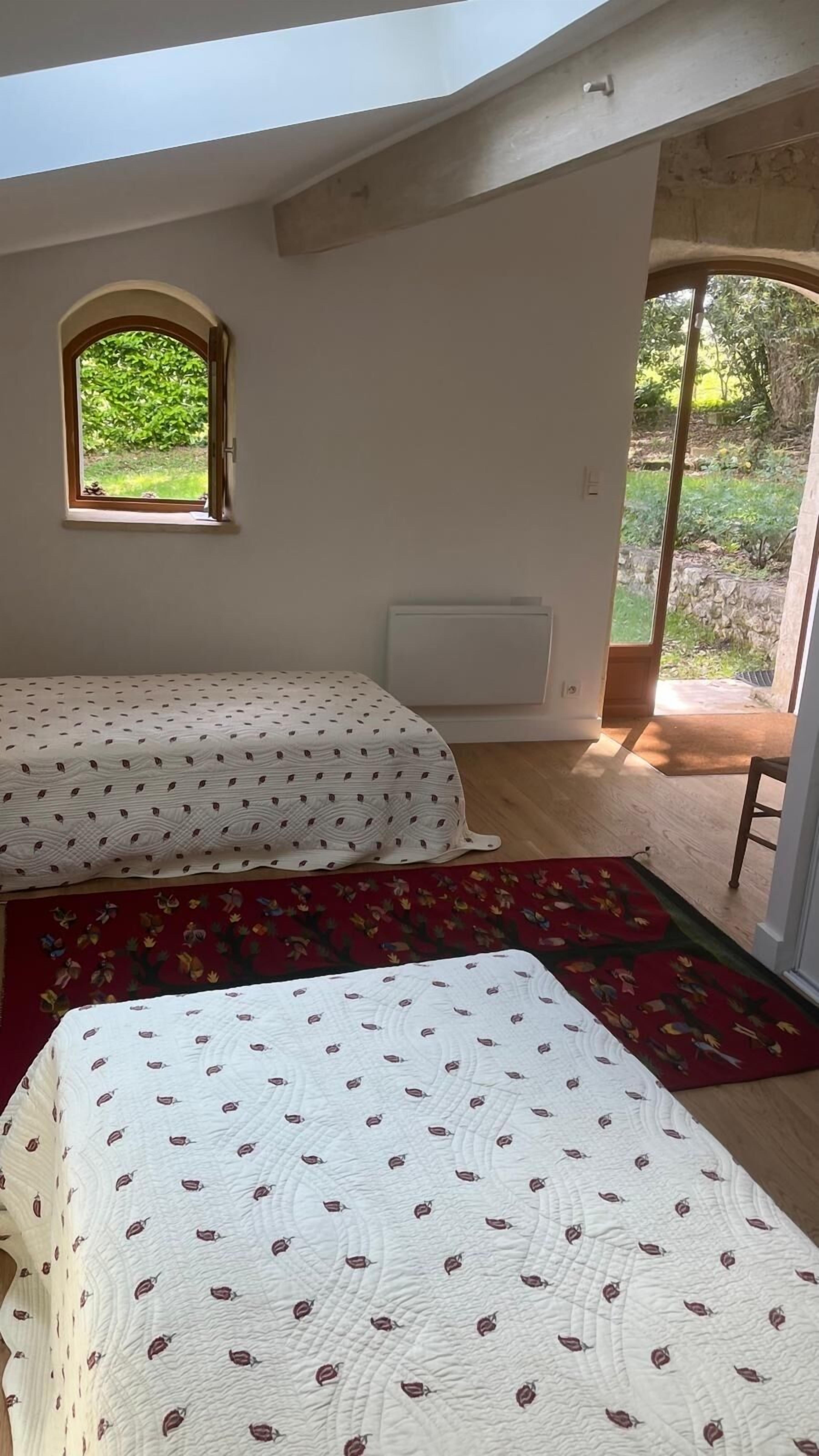 A room with two beds, a small window, and a view of greenery outside.