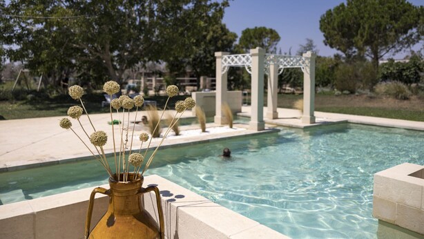 A pool with clear water, a white pergola, and a vase with dried flowers on the poolside.
