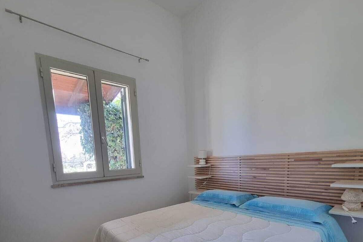 Une chambre à coucher avec un lit, une tête de lit en bois et une fenêtre donnant sur un paysage verdoyant.