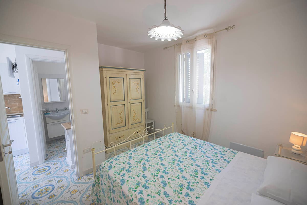 Une chambre à coucher comprenant un lit, une armoire, une fenêtre avec des rideaux et une salle de bain avec un lavabo et un miroir.