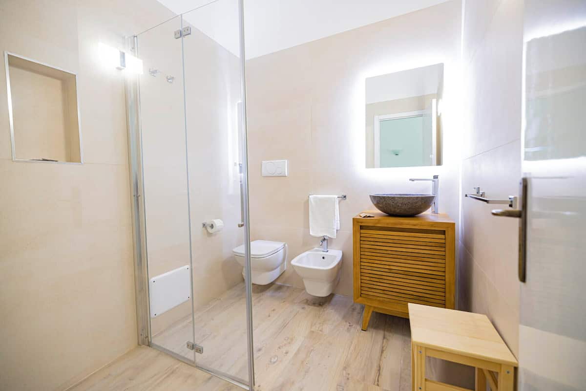 Une salle de bain moderne dotée d’une douche à parois de verre, de toilettes, d’un bidet et d’un meuble-lavabo en bois avec un lavabo en cuvette.