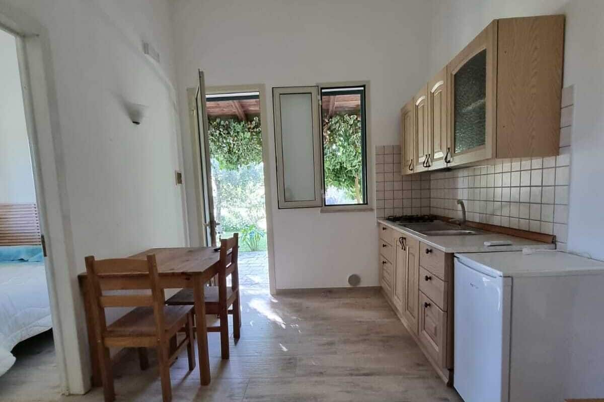 Une cuisine de taille réduite, dotée de meubles de rangement en bois, d’un réfrigérateur blanc et d’une table à manger avec des chaises.