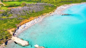 An aerial view of a coastal area with a beach, clear turquoise waters, and lush greenery.
