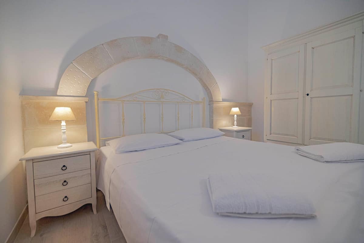 Un lit bien fait, avec du linge de lit blanc, une tête de lit en bois et deux tables de chevet avec des lampes.