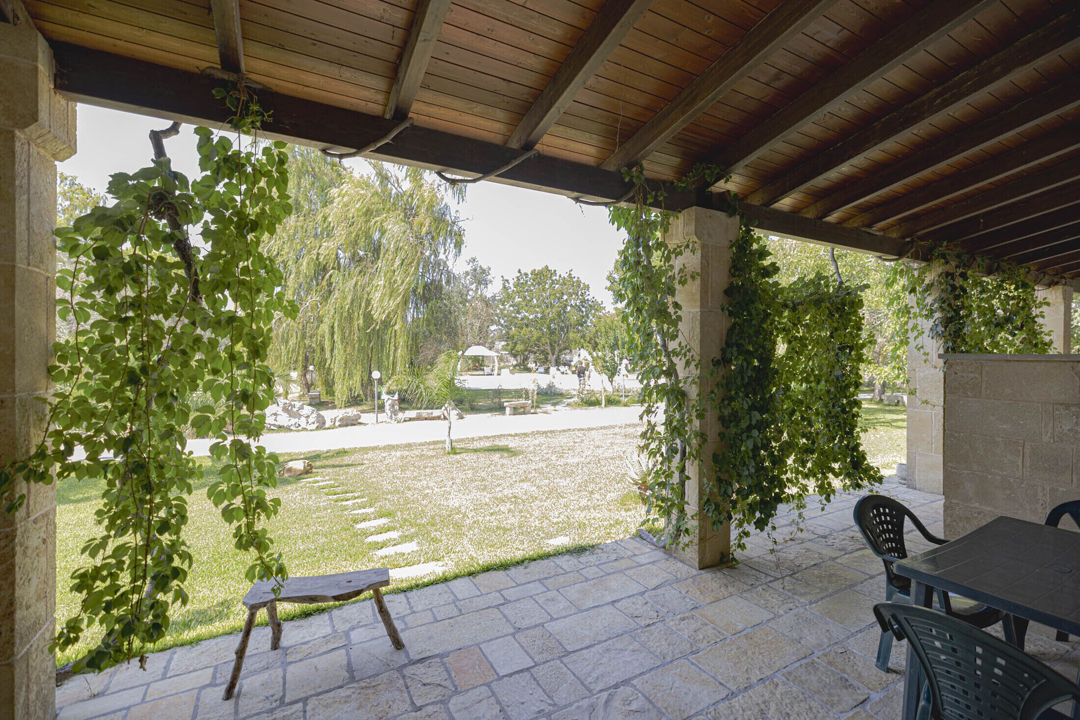 Un patio cubierto con piso de piedra, un banco de madera y una mesa con sillas.