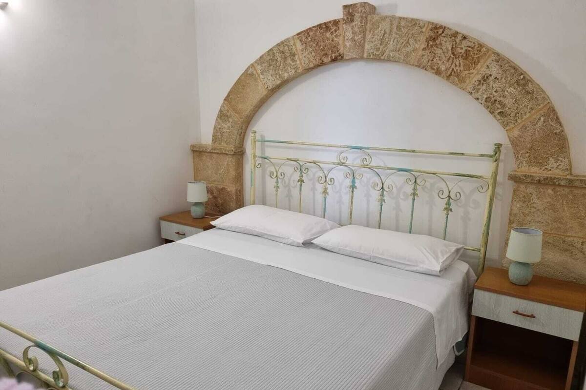 Un lit bien fait, avec une tête de lit en métal, deux tables de chevet avec des lampes et une arche en pierre au-dessus de la tête de lit.