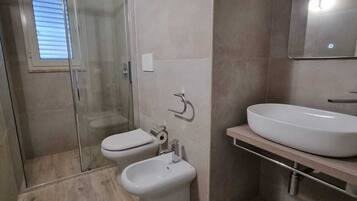 A modern bathroom with a shower, toilet, bidet, and sink.