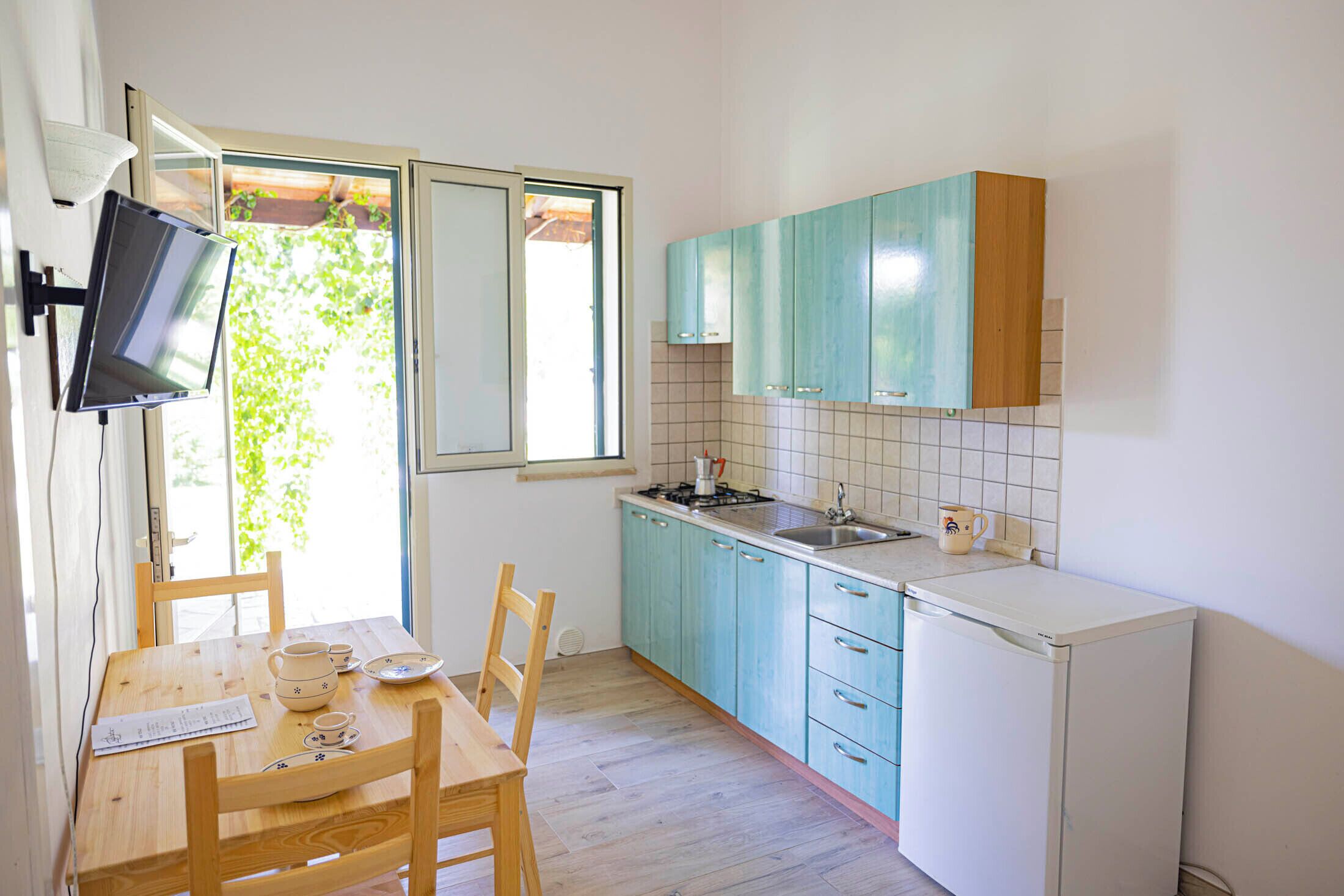 A small kitchen with teal cabinets, a white refrigerator, and a dining table with chairs.