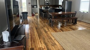 Una cucina moderna con pavimento in legno, elettrodomestici in acciaio inossidabile e un'area pranzo con tavolo e sedie in legno.