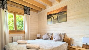 Ein Schlafzimmer mit einem großen Bett, einem Holz-Kopfschild, einem Sonnenuntergangsbild, einem Fenster mit Vorhängen und einem Nachttisch mit Lampe.