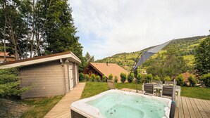 Ein Whirlpool auf einer Holzterrasse mit Blick auf eine Hügelkuppe und eine kleine Holzhütte.