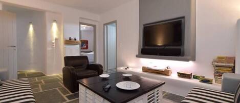A modern living room with a flat-screen TV, a coffee table, a sofa, and a chair.